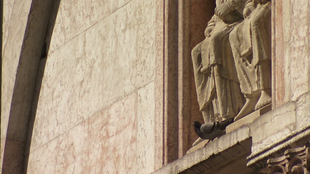 一只鸟栖息在帕尔马大教堂洗礼堂正面的一座雕像脚下。高清。视频下载