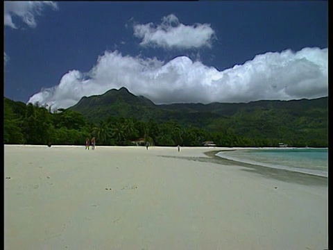 白色的沙滩与柔和的蓝绿色的海和绿色的岛屿山在背景盘留给游客在海滩上行走与大白色蓬松的云在蓝天马埃岛视频下载