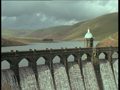 水在多云的天空下流经Elan山谷大坝，绿色的山在背景，威尔士视频素材