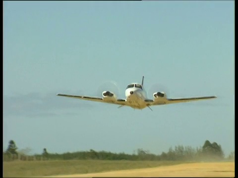 一架轻型飞机沿着布满灰尘的跑道朝着摄像机起飞，飞机的轮子折叠成起落架视频下载
