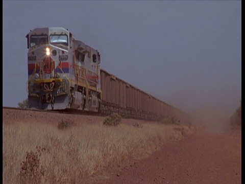 在澳大利亚沙漠的热霾中，一列货运列车接近并通过相机左侧视频下载
