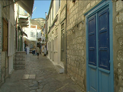一位希腊妇女走在狭窄的鹅卵石街道上视频素材