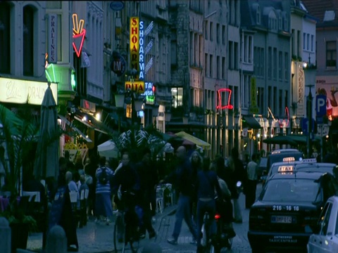 在安特卫普繁忙的街道上，人们走过或骑着自行车经过霓虹灯和店铺视频素材