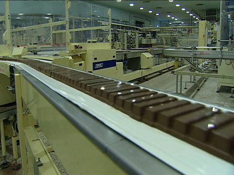 巧克力棒沿着传送带传递，工厂工人扫视生产线视频下载