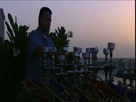 夕阳西下的迪拜，酒店老板把包裹着锡箔的陶瓷头放在屋顶咖啡馆外的水烟管上视频素材