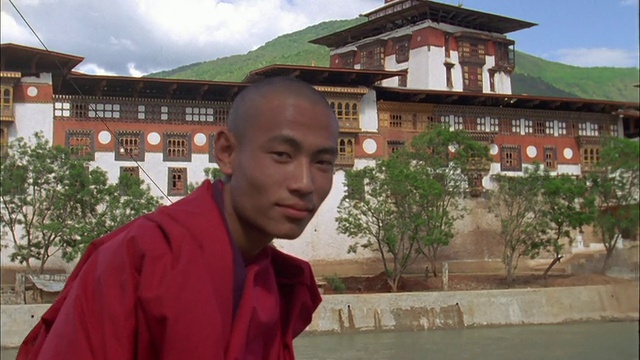 三个年轻的西藏僧人坐在寺庙外的水道附近。高清。视频下载