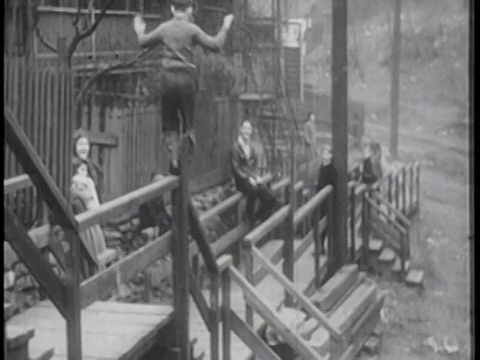 1939年，一个男孩在室外滑下楼梯栏杆，其他孩子和成年人在观看/纪录片视频素材