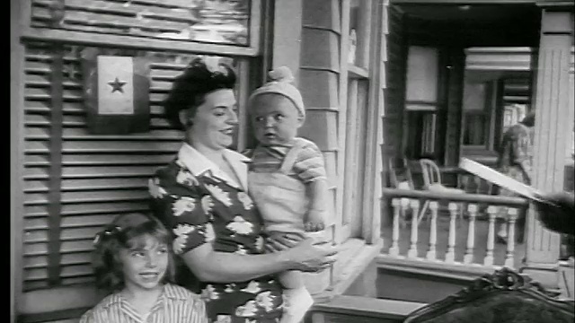 1944年，一名妇女在前廊抱着婴儿和女儿站在递给她的信封旁视频素材