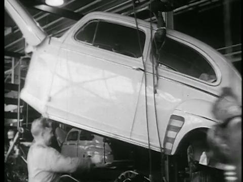 B/W 1945年汽车工人在汽车装配线上用绳索引导车身视频素材