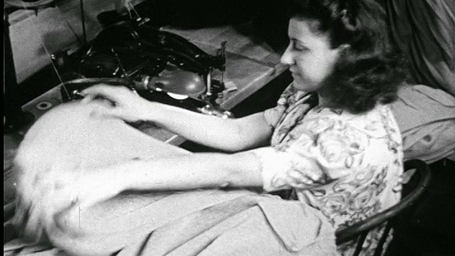 1946年，一名妇女坐在缝纫机旁把毛衣堆在制衣厂视频素材