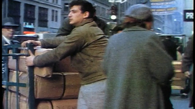 1957年，两名男子在拥挤的城市人行道上推着车，一名男子骑着一辆装着箱子的手推车视频下载