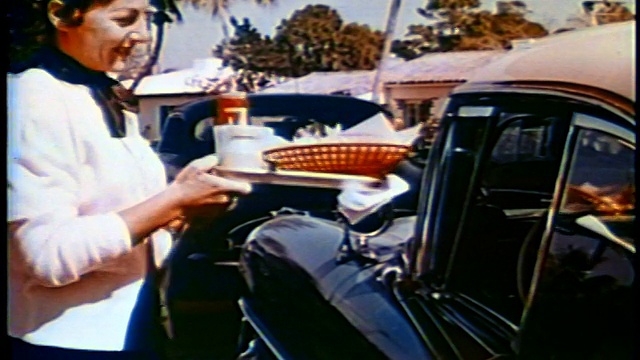 1958年，一名女服务员将一盘食物放在免下车餐厅的汽车窗台上/新闻短片视频下载