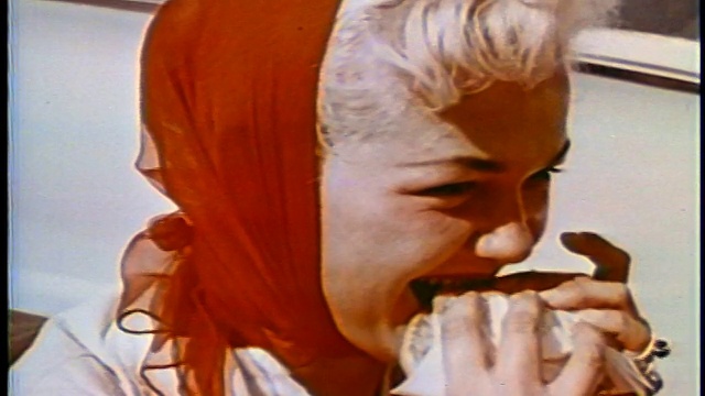 1958年近距离观察头上戴着红围巾的金发女人在户外吃汉堡包/新闻片视频下载