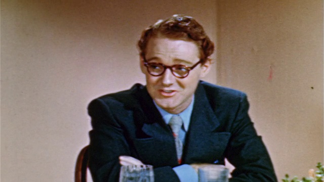 1952年，一位戴眼镜的红发青年坐在桌边与银幕外的人交谈视频素材