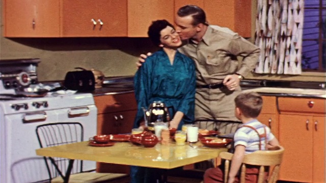 1957年，一名穿着长袍的妇女把咖啡壶端到餐桌上+倒牛奶/一名男子亲吻她的脸颊视频下载