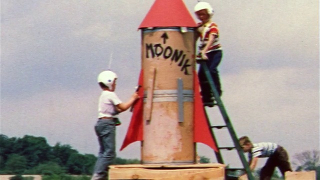 1959年2个带着塑料头盔的男孩在自制的大型玩具火箭上工作/男孩推着另一个在玩具车上视频素材
