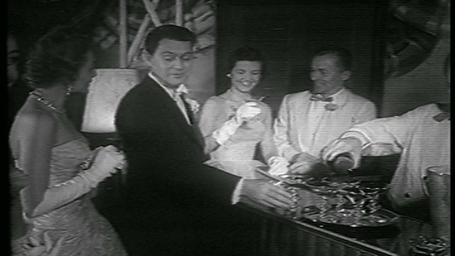 1953年，一名身着燕尾服的男子在酒吧向身着正式礼服的女子递上香槟视频素材