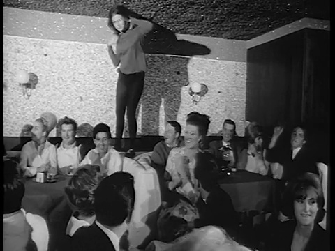 1965年B/W女人穿着黑色紧身衣跳舞在夜总会的桌子上，人群鼓掌/新闻短片视频素材