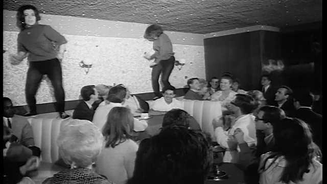1965年，两个穿着黑色紧身衣的女人在夜总会的桌子上跳舞，人群鼓掌/新闻短片视频素材
