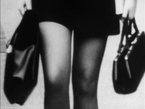 20世纪60年代的B/W超短裙将女人的腿收起来，走向相机/拿着钱包/新闻胶片视频下载