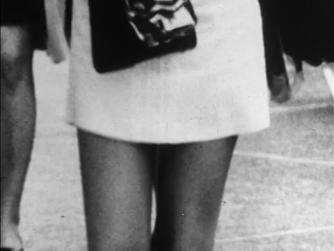 60年代的B/W超短裙遮住女人的双腿走在人行道上/拿着钱包/新闻短片视频下载