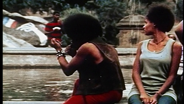 长着非洲式发式的黑人坐在喷泉边/倾斜到脚/一群嬉皮士视频素材
