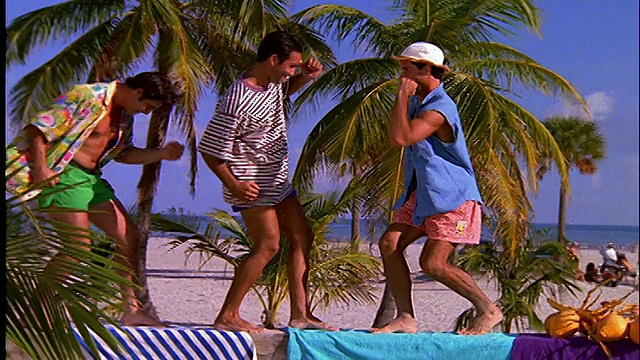 3个男人在沙滩上的长椅上跳舞/傻乎乎地走着视频素材