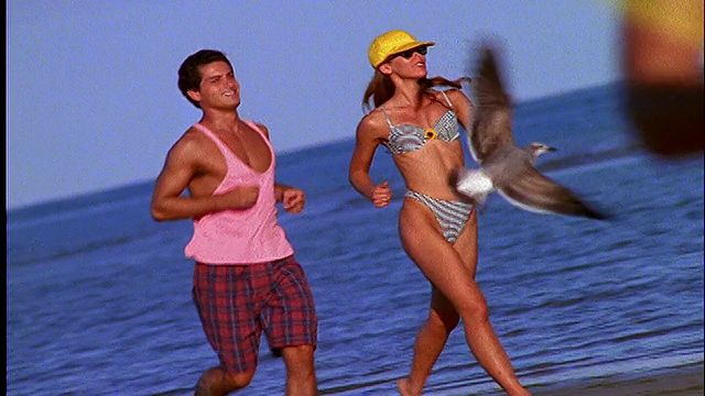 一对穿着泳衣在海滩上慢跑的夫妇视频素材