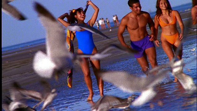 一群穿着泳衣的人在沙滩上跑步的慢镜头视频素材