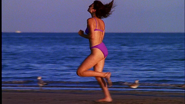 穿着比基尼的女人在海滩上跑步/经过2个男人视频素材