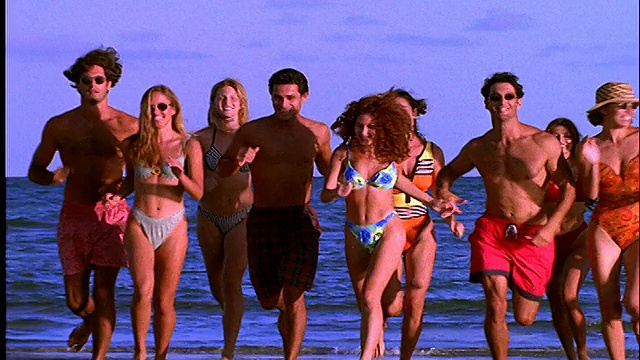 一群穿着泳衣的人在海滩上向cam跑去视频素材