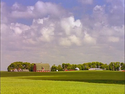 宽镜头延时云在蓝色的天空在绿色的田野和红色的农场建筑的背景/曼尼托巴的布兰登视频素材