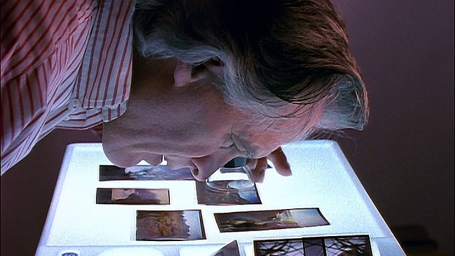 一个白发苍苍的人用放大镜仔细检查片子视频素材