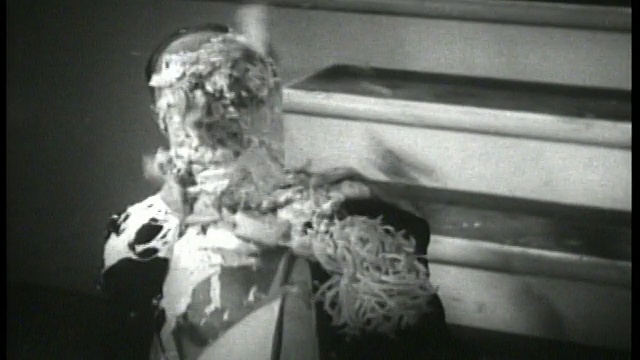 1930年的近镜头，一名穿着燕尾服的男子坐在地板上，被派砸到脸上视频素材