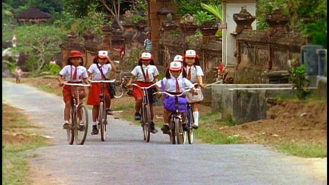 慢镜头，一群穿着制服的女学生骑着自行车在乡村公路上走向相机/巴厘岛视频下载