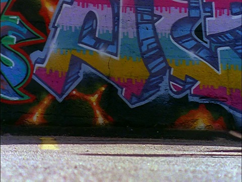 慢动作接近滑板的腿通过相机/涂鸦覆盖的墙在背景视频素材