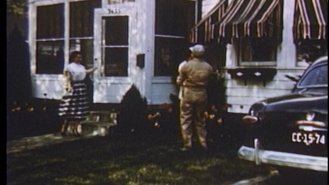 1951年，一名身穿工作服的男子在院子里将孩子举到空中，妻子走出家门迎接他/底特律视频素材