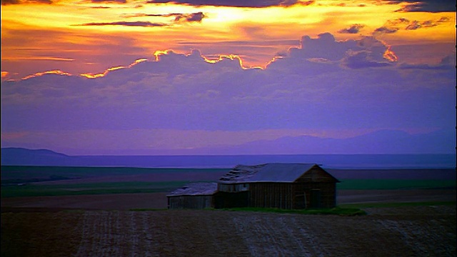 日落时分，爱达荷州田野上破旧的谷仓上空的宽镜头延时云视频素材