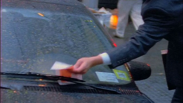 慢镜头向上倾斜，商人在雨中的纽约街道上发现汽车挡风玻璃上的停车罚单视频下载