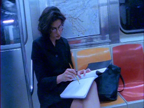 戴着眼镜的蓝色慢动作女商人坐在地铁上，在binder / NYC中写作视频素材