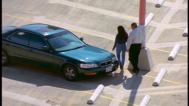 倾斜高角度放大夫妇走到汽车在空停车场/男人拥抱女人，她开车离开视频素材