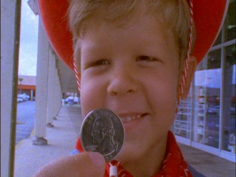 慢镜头特写微笑的金发男孩戴着牛仔帽+在镜头前举起四分之一视频下载