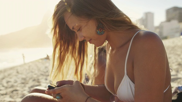 在巴西里约热内卢的伊帕内玛海滩上，一名年轻女子在她的智能手机上打字视频素材
