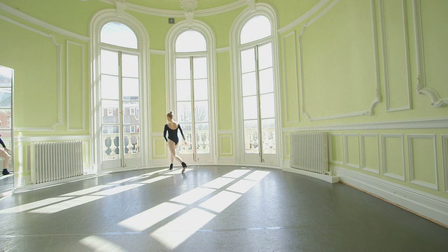 女芭蕾舞者练习她的舞蹈动作跳跃，滑翔和旋转在一个开放的工作室视频素材