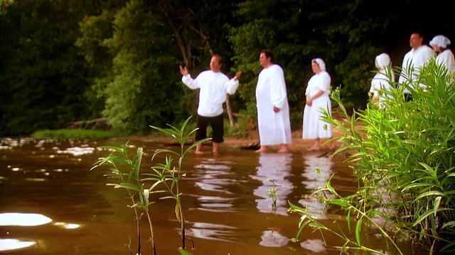 美国弗吉尼亚州费尔法克斯站，牧师在洗礼仪式上欢迎并带领着一排穿着白色衣服的人走进湖中视频下载