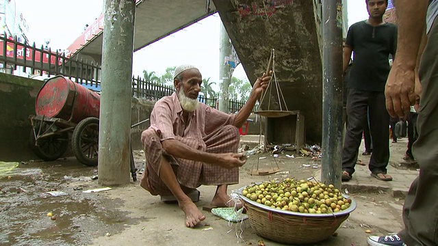 孟加拉国达卡，一名街头小贩用老式秤为两名顾客称水果视频下载