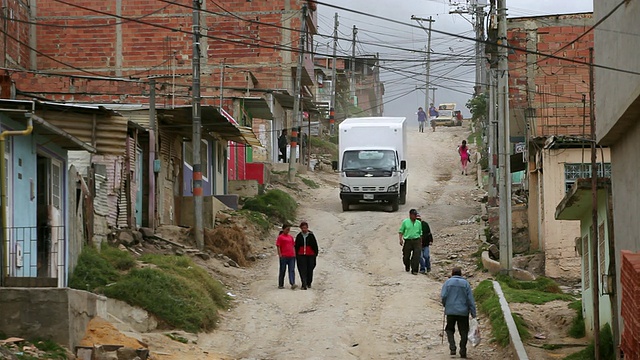哥伦比亚波哥大的Ciudad Bolivar贫民窟，卡车和行人在尘土飞扬的街道上行走视频下载