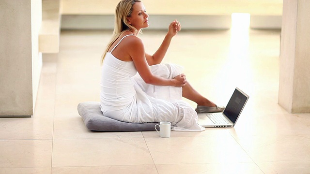 一个成熟的女人坐在地板上拿着笔记本电脑视频素材