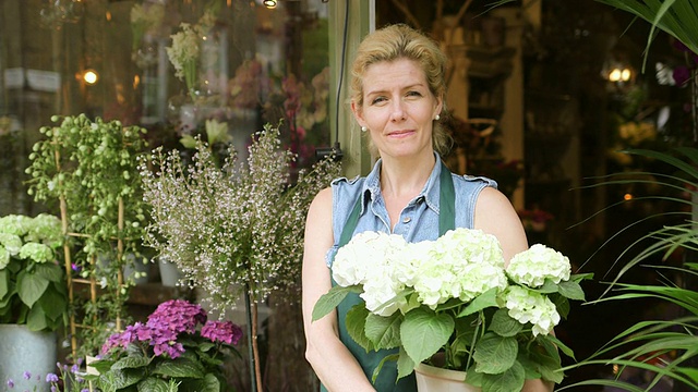 一位高级花商站在她的商店门口，骄傲地欣赏着她的花视频素材