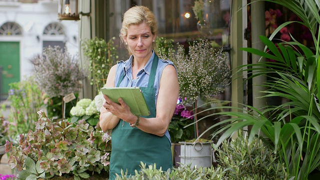 一位高级花商站在她的店铺门口，一边看花，一边在平板电脑上输入信息视频素材